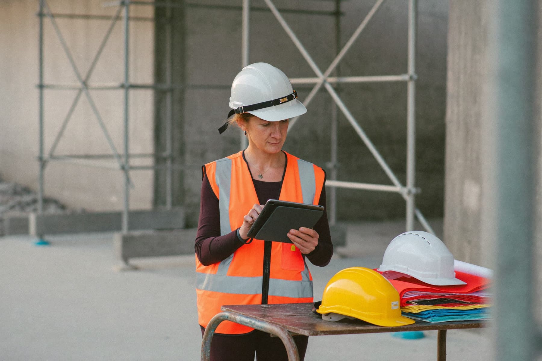 A construction company owner in a hard hat and safety vest reviewing plans on a tablet at a building site
