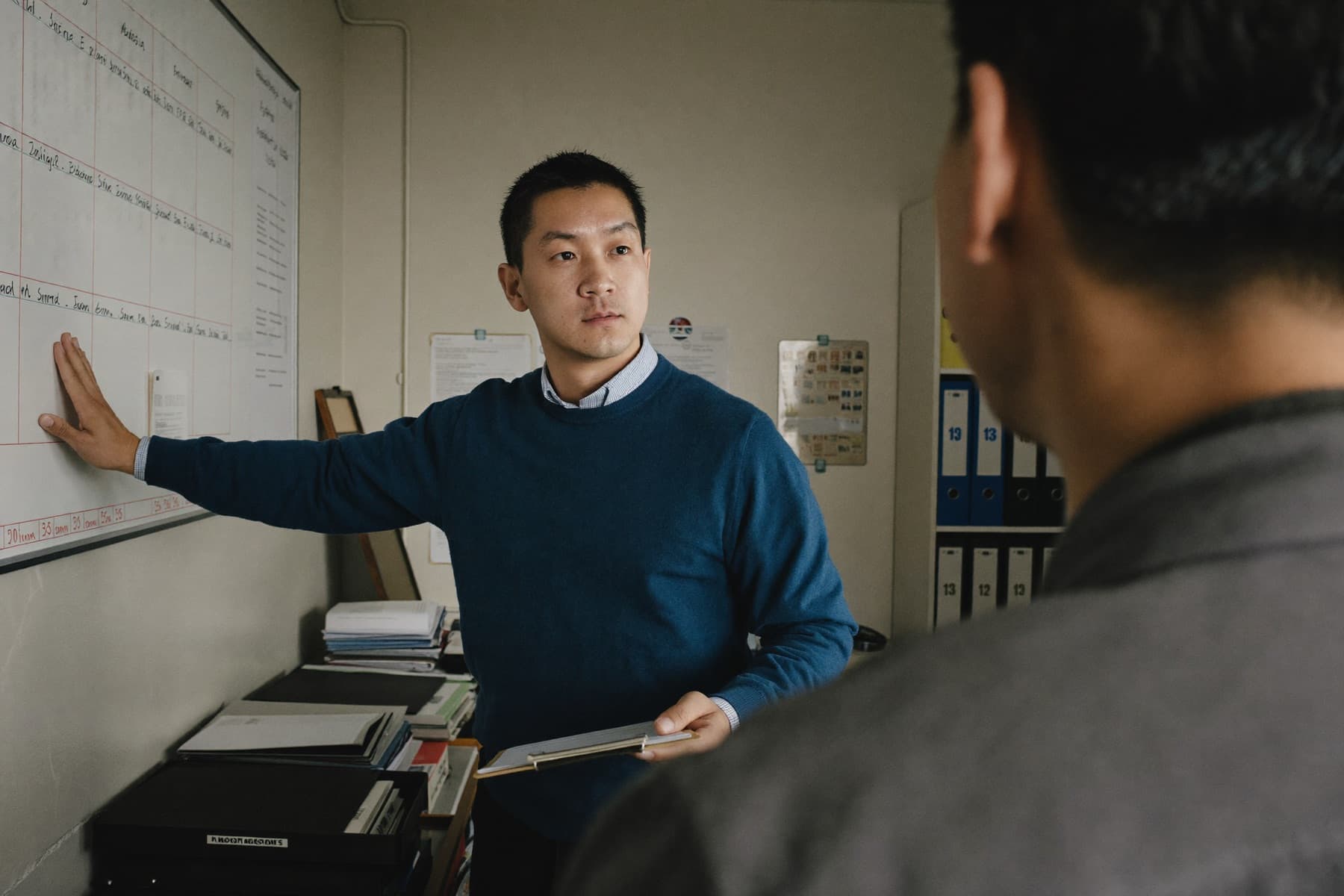 A facilities company owner at a whiteboard schedule, talking with a colleague