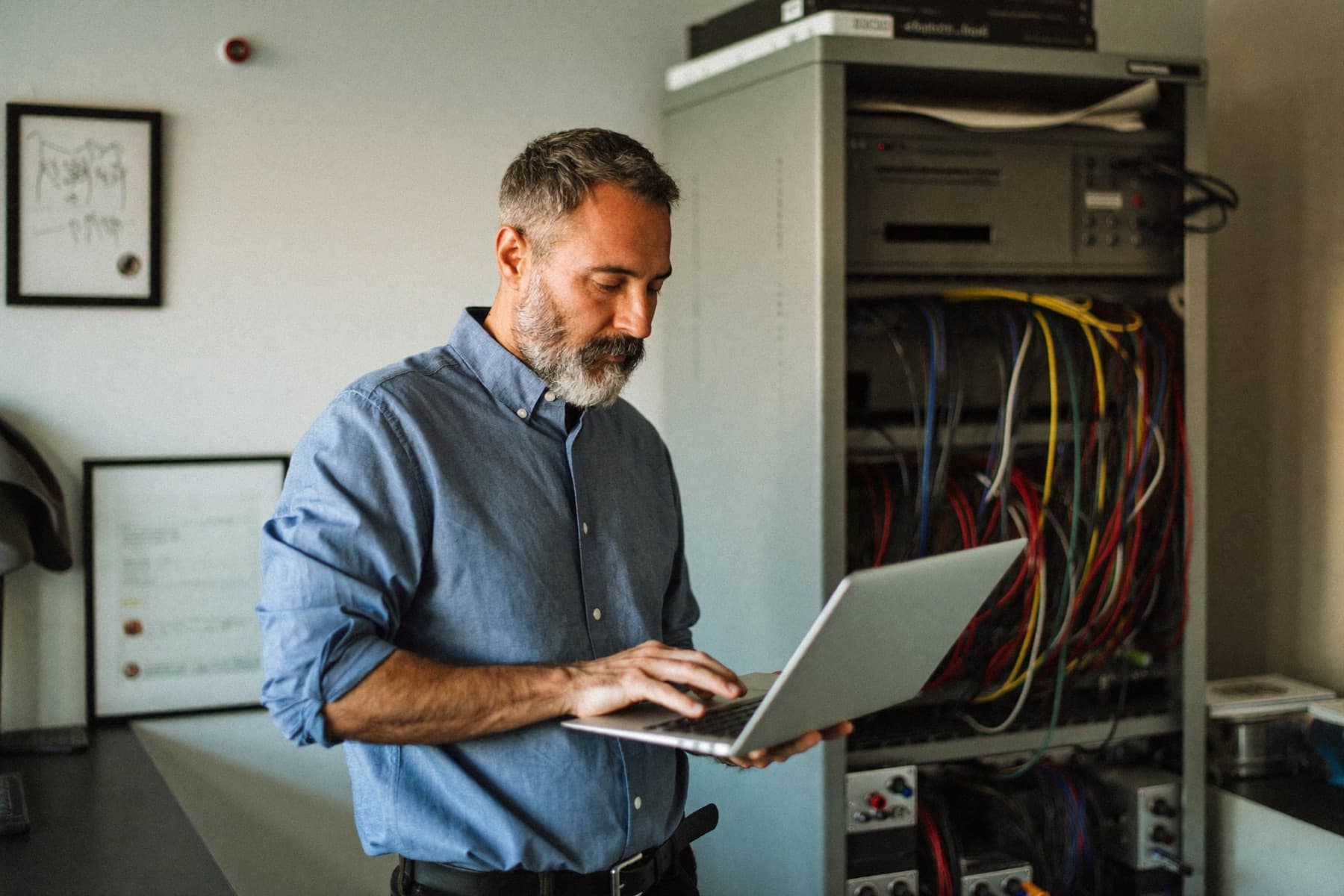 An IT services owner with a laptop beside a small server rack in his office
