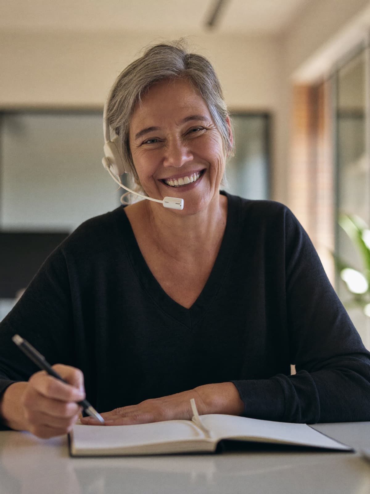 A smiling adviser in a headset on a video call, a notebook open on her desk