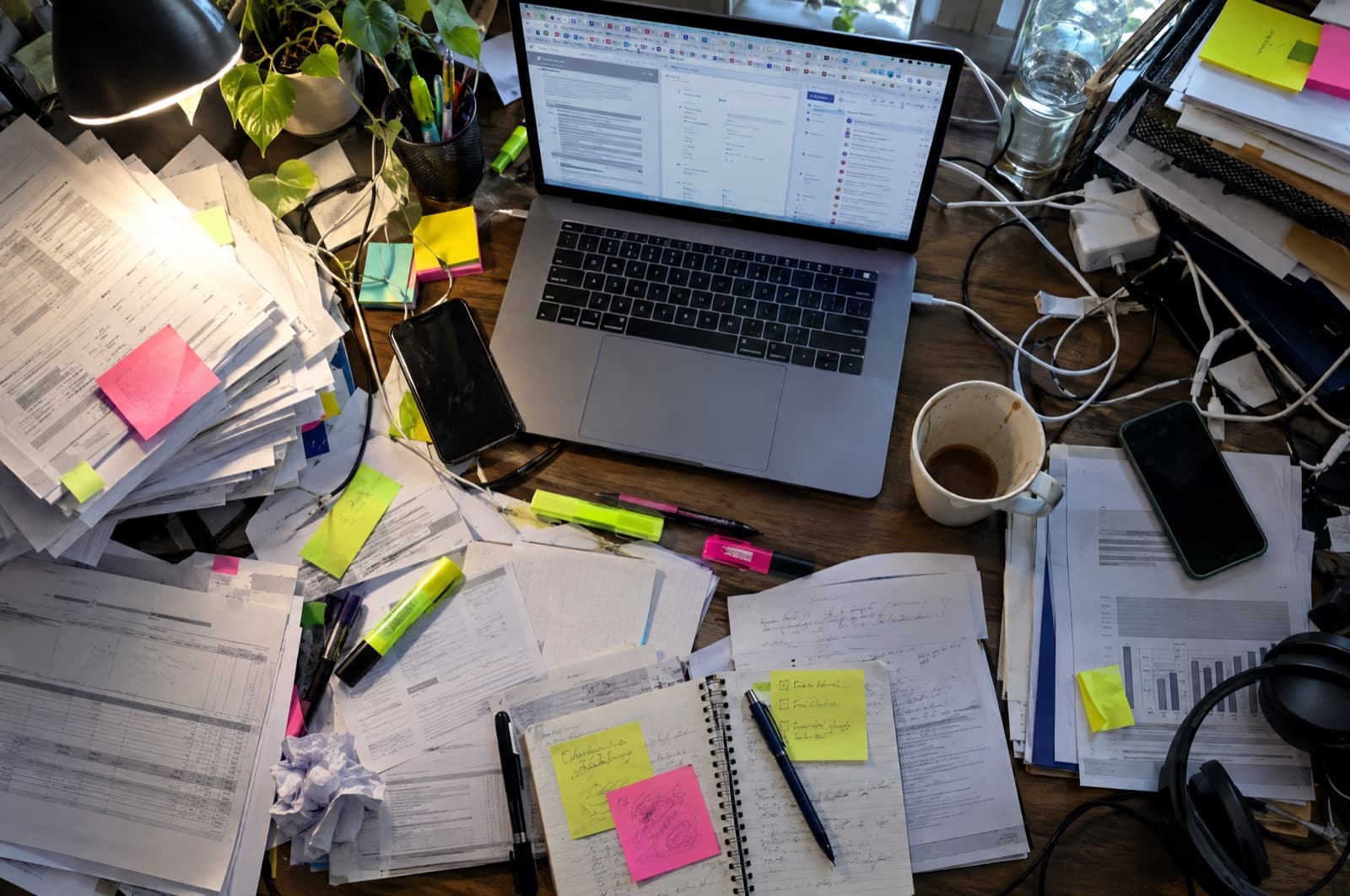 A desk buried in printouts, sticky notes and open browser tabs